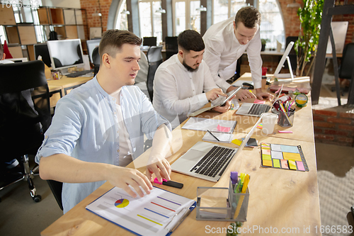 Image of Young caucasian colleagues working together in a office using modern devices and gadgets