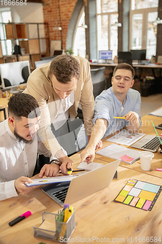Image of Young caucasian colleagues working together in a office using modern devices and gadgets