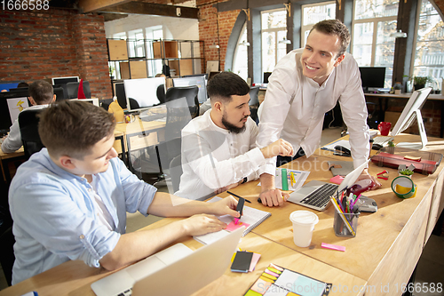 Image of Young caucasian colleagues working together in a office using modern devices and gadgets