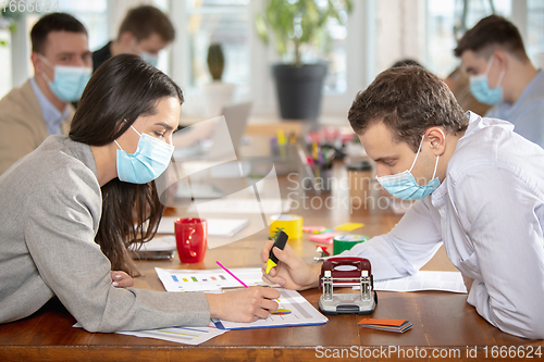 Image of Side view colleagues working together in face masks during quarantine in a office using modern devices and gadgets during creative meeting