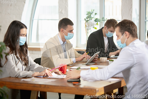 Image of Side view colleagues working together in face masks during quarantine in a office using modern devices and gadgets during creative meeting