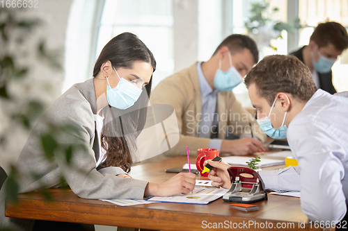 Image of Side view colleagues working together in face masks during quarantine in a office using modern devices and gadgets during creative meeting