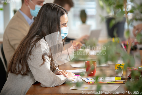 Image of Side view colleagues working together in face masks during quarantine in a office using modern devices and gadgets during creative meeting