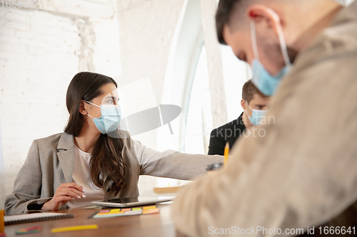 Image of Side view colleagues working together in face masks during quarantine in a office using modern devices and gadgets during creative meeting