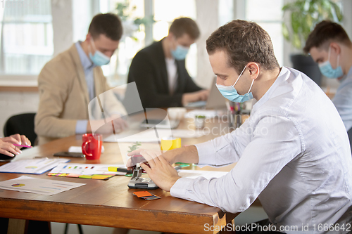 Image of Side view colleagues working together in face masks during quarantine in a office using modern devices and gadgets during creative meeting