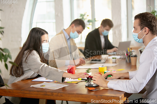 Image of Side view colleagues working together in face masks during quarantine in a office using modern devices and gadgets during creative meeting