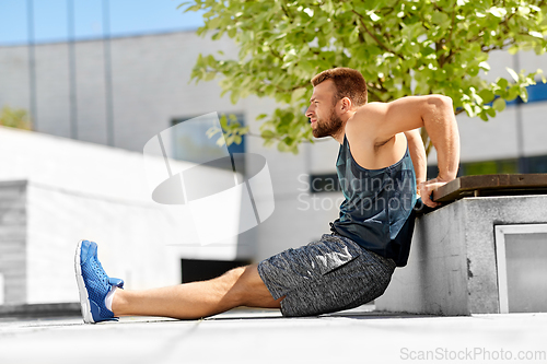 Image of young man doing triceps dip on city street