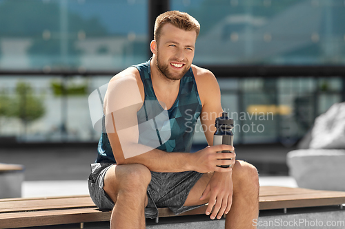 Image of happy sportsman with bottle sitting on city bench