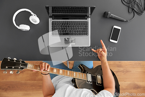 Image of young man with laptop playing guitar at table