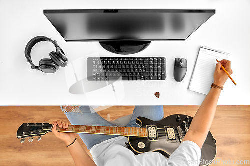 Image of man with guitar writing to music book at table