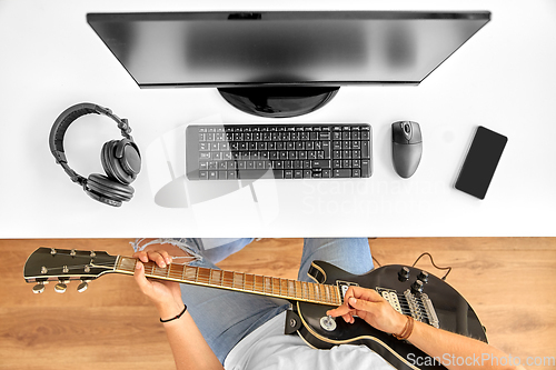 Image of young man with computer playing guitar at table