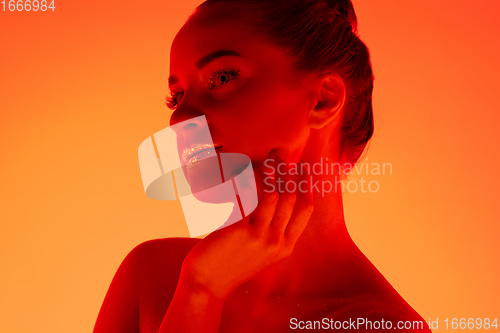 Image of Handsome woman\'s portrait isolated on orange gradient studio background in neon light, monochrome