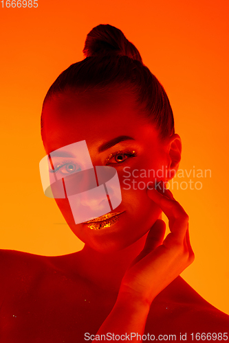 Image of Handsome woman\'s portrait isolated on orange gradient studio background in neon light, monochrome
