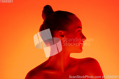 Image of Handsome woman\'s portrait isolated on orange gradient studio background in neon light, monochrome