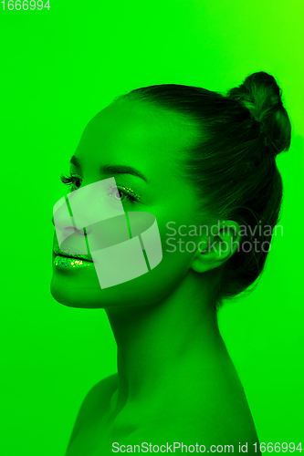 Image of Handsome woman\'s portrait isolated on green studio background in neon light, monochrome