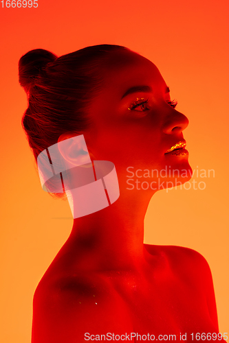 Image of Handsome woman\'s portrait isolated on orange gradient studio background in neon light, monochrome