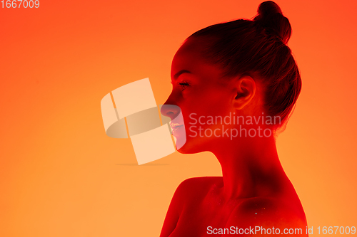 Image of Handsome woman\'s portrait isolated on orange gradient studio background in neon light, monochrome