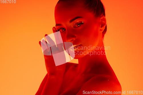 Image of Handsome woman\'s portrait isolated on orange gradient studio background in neon light, monochrome