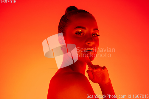 Image of Handsome woman\'s portrait isolated on orange gradient studio background in neon light, monochrome