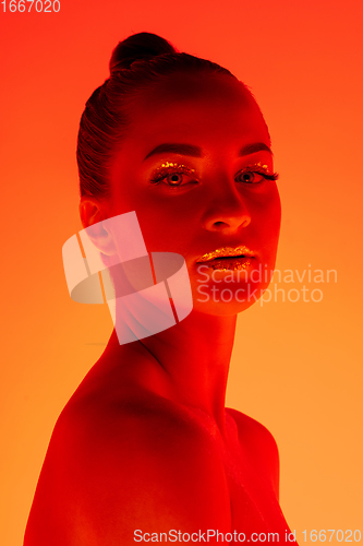Image of Handsome woman\'s portrait isolated on orange gradient studio background in neon light, monochrome