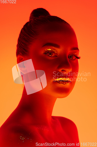 Image of Handsome woman\'s portrait isolated on orange gradient studio background in neon light, monochrome