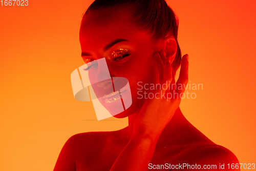 Image of Handsome woman\'s portrait isolated on orange gradient studio background in neon light, monochrome