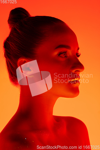 Image of Handsome woman\'s portrait isolated on orange gradient studio background in neon light, monochrome