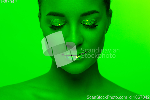 Image of Handsome woman\'s portrait isolated on green studio background in neon light, monochrome