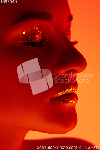 Image of Handsome woman\'s portrait isolated on orange gradient studio background in neon light, monochrome