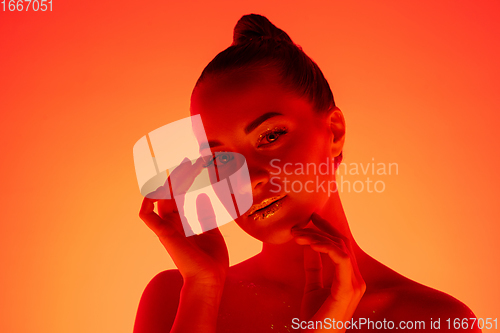 Image of Handsome woman\'s portrait isolated on orange gradient studio background in neon light, monochrome