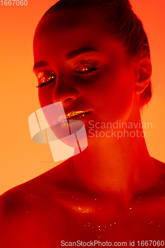 Image of Handsome woman\'s portrait isolated on orange gradient studio background in neon light, monochrome