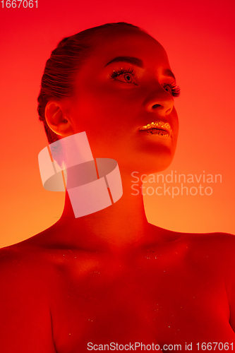 Image of Handsome woman\'s portrait isolated on orange gradient studio background in neon light, monochrome