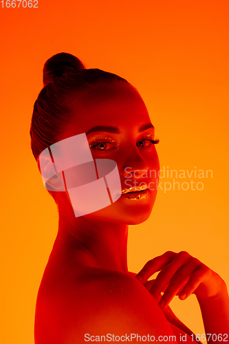 Image of Handsome woman\'s portrait isolated on orange gradient studio background in neon light, monochrome