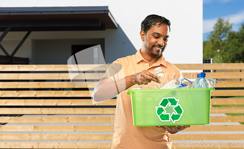 Image of smiling young indian man sorting plastic waste