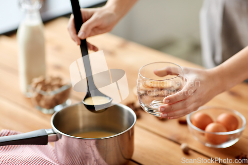 Image of hands with ladle pouring eggnog from pot to glass