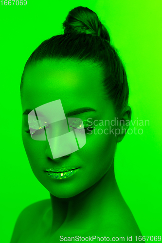 Image of Handsome woman\'s portrait isolated on green studio background in neon light, monochrome