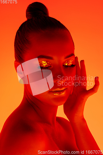 Image of Handsome woman\'s portrait isolated on orange gradient studio background in neon light, monochrome