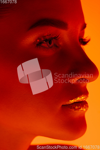 Image of Handsome woman\'s portrait isolated on orange gradient studio background in neon light, monochrome