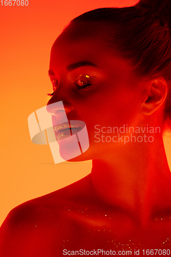 Image of Handsome woman\'s portrait isolated on orange gradient studio background in neon light, monochrome