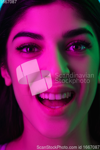 Image of Brunette beautiful woman\'s portrait isolated on blue studio background in multicolored neon light