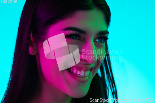Image of Brunette beautiful woman\'s portrait isolated on blue studio background in multicolored neon light