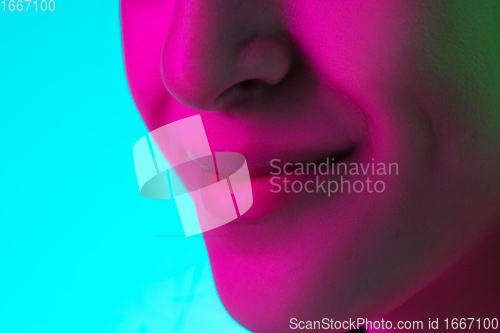 Image of Close up beautiful woman\'s smile isolated on blue studio background in multicolored neon light