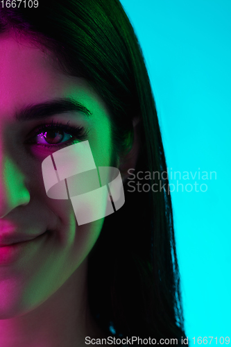 Image of Brunette beautiful woman\'s portrait isolated on blue studio background in multicolored neon light