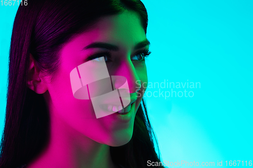 Image of Brunette beautiful woman\'s portrait isolated on blue studio background in multicolored neon light