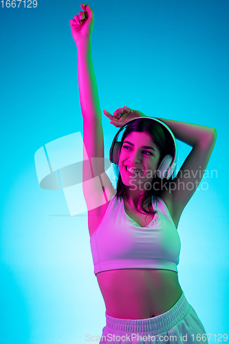 Image of Brunette beautiful woman\'s portrait isolated on blue studio background in multicolored neon light