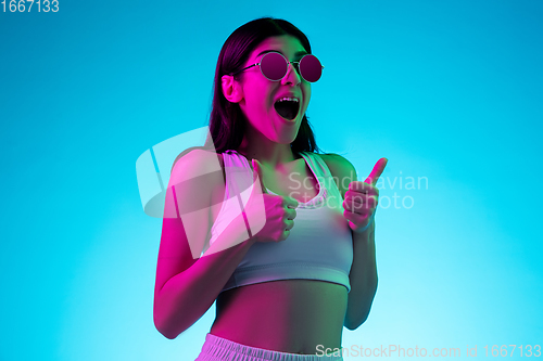 Image of Brunette beautiful woman\'s portrait isolated on blue studio background in multicolored neon light