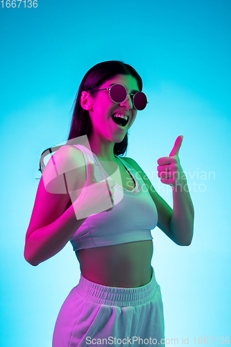 Image of Brunette beautiful woman\'s portrait isolated on blue studio background in multicolored neon light