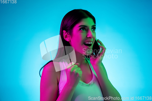 Image of Brunette beautiful woman\'s portrait isolated on blue studio background in multicolored neon light. Talking phone.