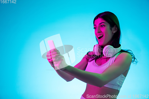 Image of Brunette beautiful woman\'s portrait isolated on blue studio background in multicolored neon light