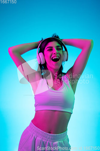 Image of Brunette beautiful woman\'s portrait isolated on blue studio background in multicolored neon light